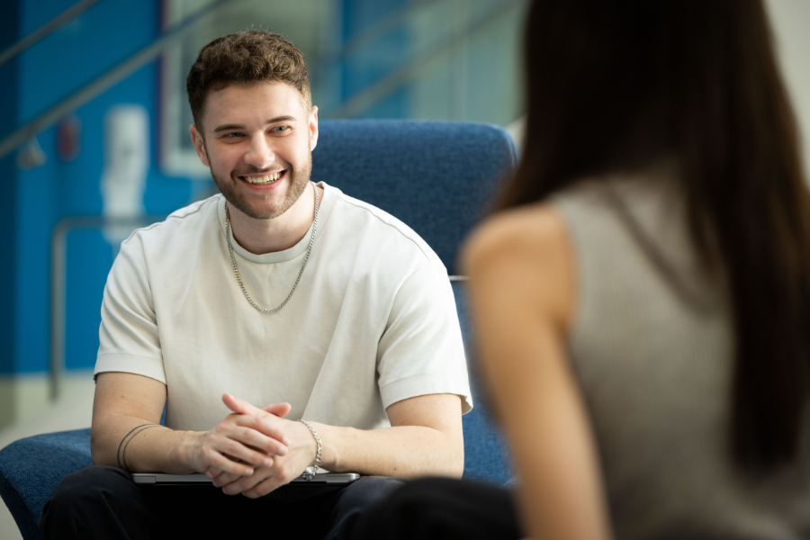 Two LMU students sit in chairs talking in LMU's Von der Ahe building.